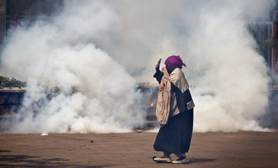 An elderly woman caught up in the clashes holds her hands in the air as a riot policeman approach amidst clouds of tear gas, during a protest in downtown Nairobi, Kenya, May 16, 2016. Kenyan police have tear-gassed and beaten opposition supporters during a protest demanding the disbandment of the electoral authority over alleged bias and corruption. (AP Photo/Ben Curtis)