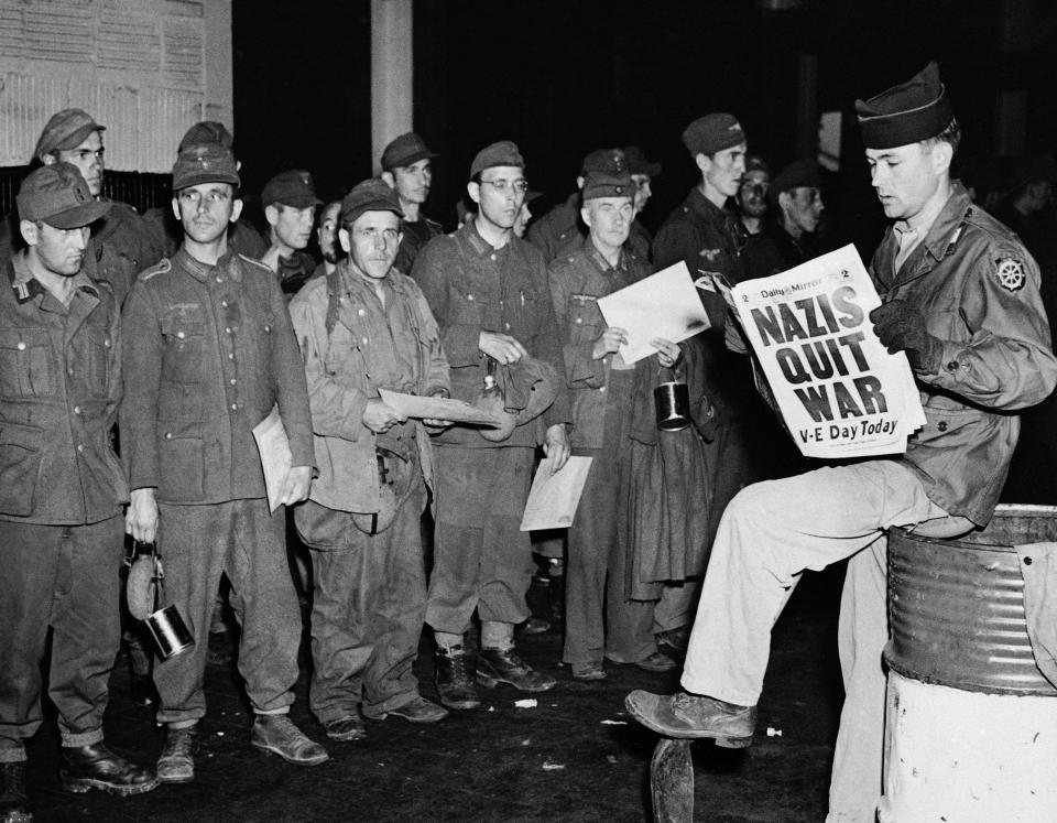 FILE - In this May 8, 1945 file photo Pfc. Clarence K. Ayers of Evansville, Ind., reads the news of VE Day as newly arrived German prisoners stand on a New York City pier. (AP Photo/John Rooney, File)