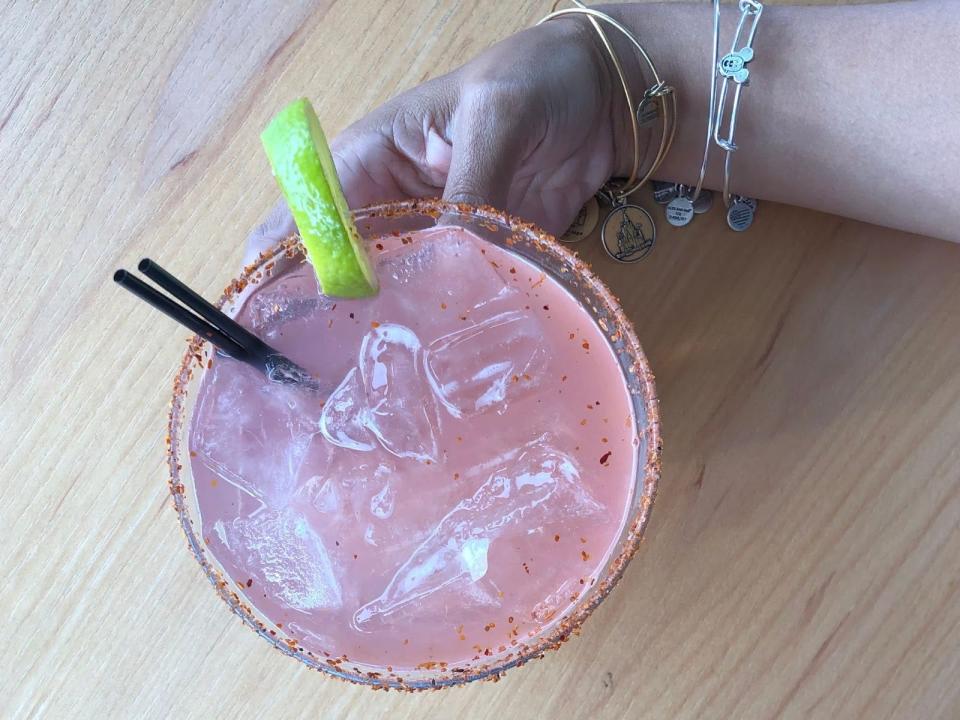 A pink margarita with two small, black straws and a lime