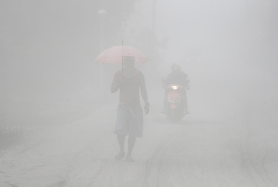 In this Monday, Jan. 13, 2020, photo, a man walks through a cloud of volcanic ash as he evacuates to safer grounds as Taal volcano in Lemery, Batangas province, southern Philippines. Red-hot lava is gushing from the volcano after a sudden eruption of ash and steam that forced residents to flee and shut down Manila’s airport, offices and schools. (AP Photo/Aaron Favila)