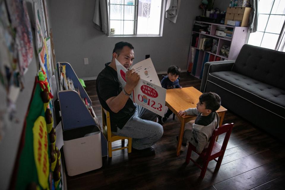 A man reads a numbers book to two boys at a Boyle Heights home day care center