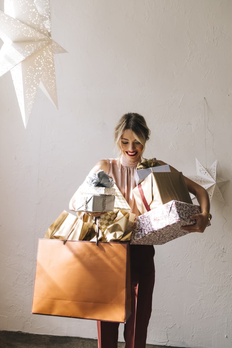 woman holding many gifts in bags and boxes and smiling. Paper stars above her as decorations