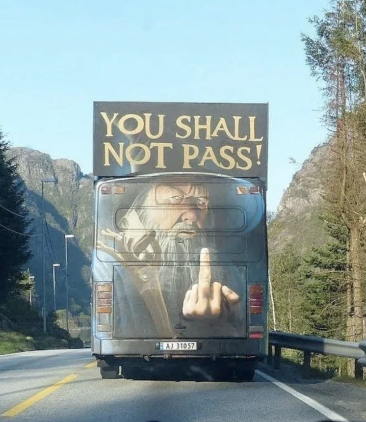 Rear of a bus with a graphic of Gandalf and text "YOU SHALL NOT PASS!" blocking a road