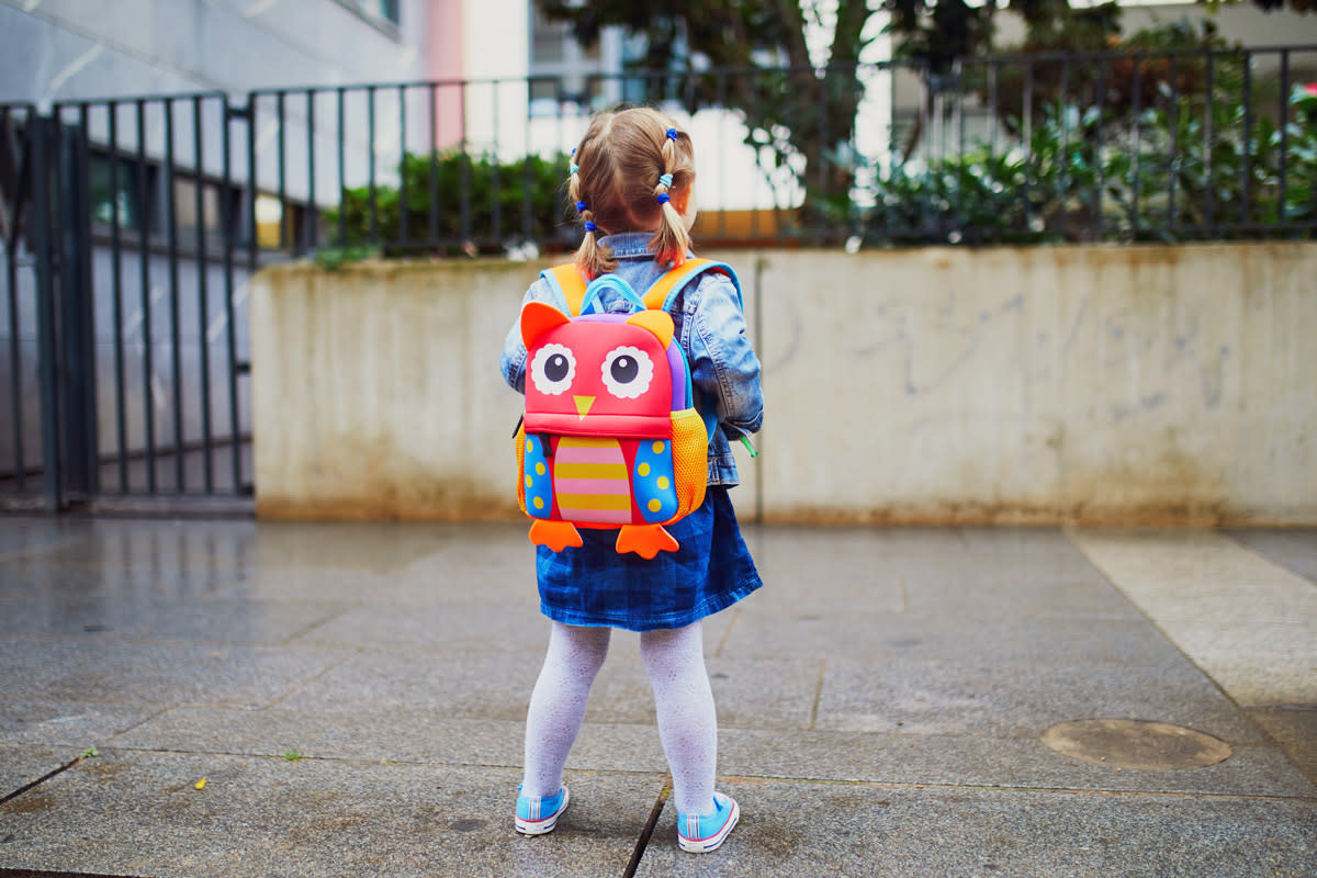 A little girl carries her owl shaped backpack. 