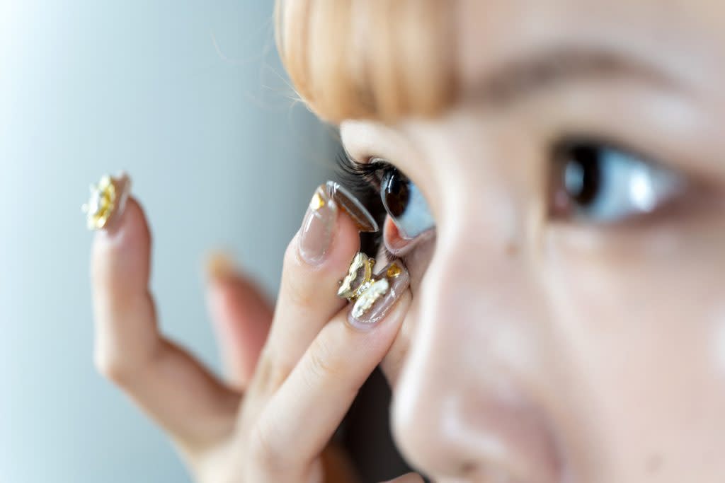 A woman puts a contact in her eye. 