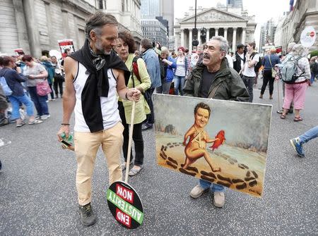 A demonstrator looks at an artist holding a painting showing Britain's Chancellor George Osborne, during an anti-austerity protest in London, Britain June 20, 2015. REUTERS/Suzanne Plunkett