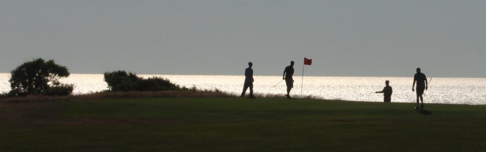 Golfers on a green at Highland Links, with the Atlantic Ocean shimmering in the distance.