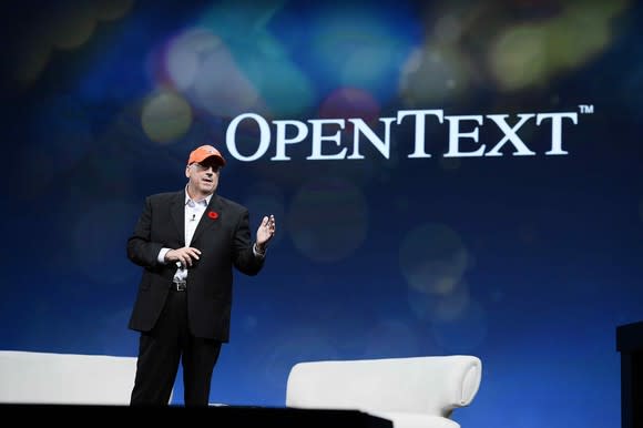 CEO Mark Barrenechea standing in front of a backdrop with the OpenText logo on it.