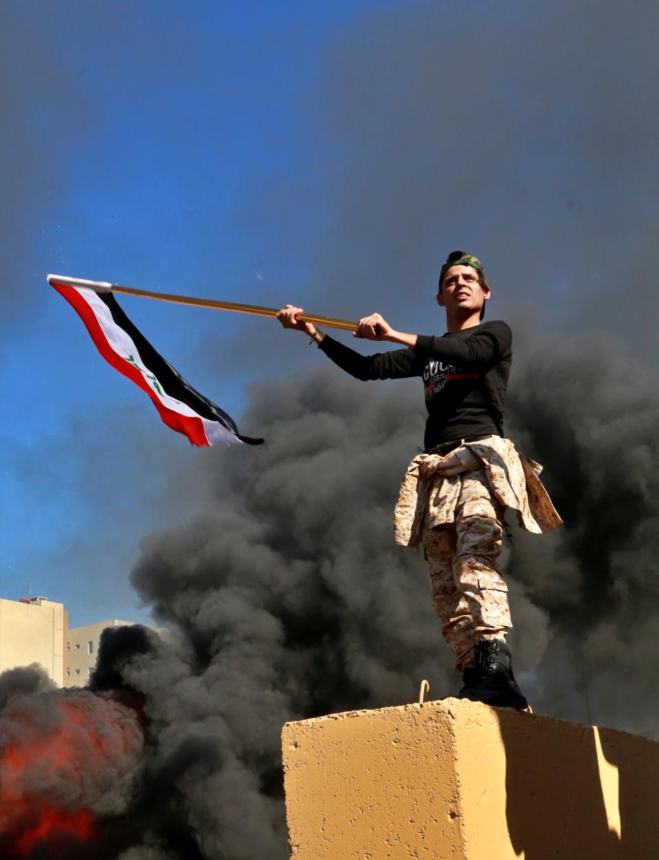 Protesters burn property as a militiaman waves an Iraqi flag in front of the U.S. embassy compound, in Baghdad, Iraq, Tuesday, Dec. 31, 2019. Dozens of angry Iraqi Shiite militia supporters broke into the U.S. Embassy compound in Baghdad on Tuesday after smashing a main door and setting fire to a reception area, prompting tear gas and sounds of gunfire. (AP Photo/Khalid Mohammed)