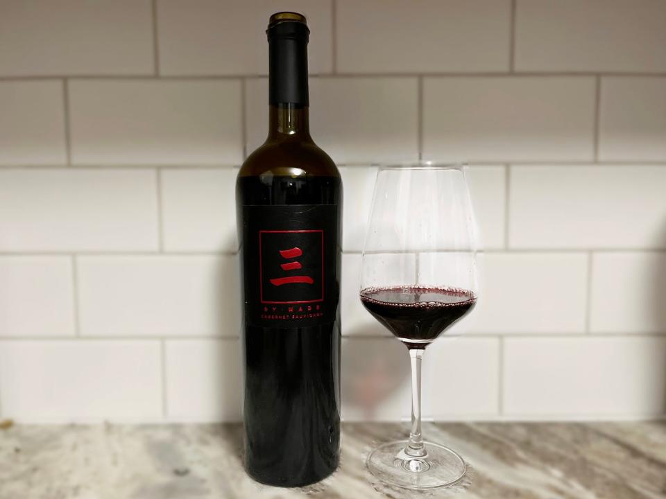 A bottle of Dwyane Wade's Three by Wade Cabernet Sauvignon sits next to a glass on a counter.