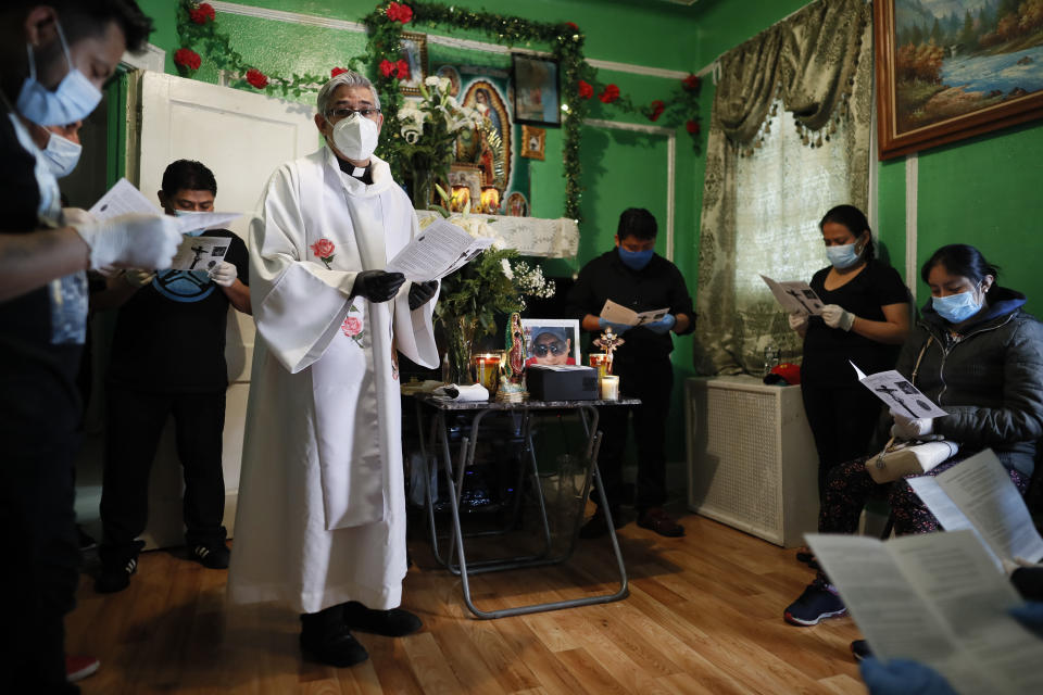 The Rev. Fabian Arias leads a prayer as he performs an in-home service beside the remains of Raul Luis Lopez who died from COVID-19 the previous month, Saturday, May 9, 2020, in the Corona neighborhood of the Queens borough of New York. (AP Photo/John Minchillo)