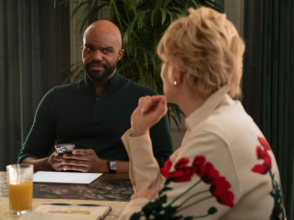 carl clemons-hopkins as marcus in hacks. they're wearing a greens shirt and looking skeptically down a table at deborah vance, played by jean smart