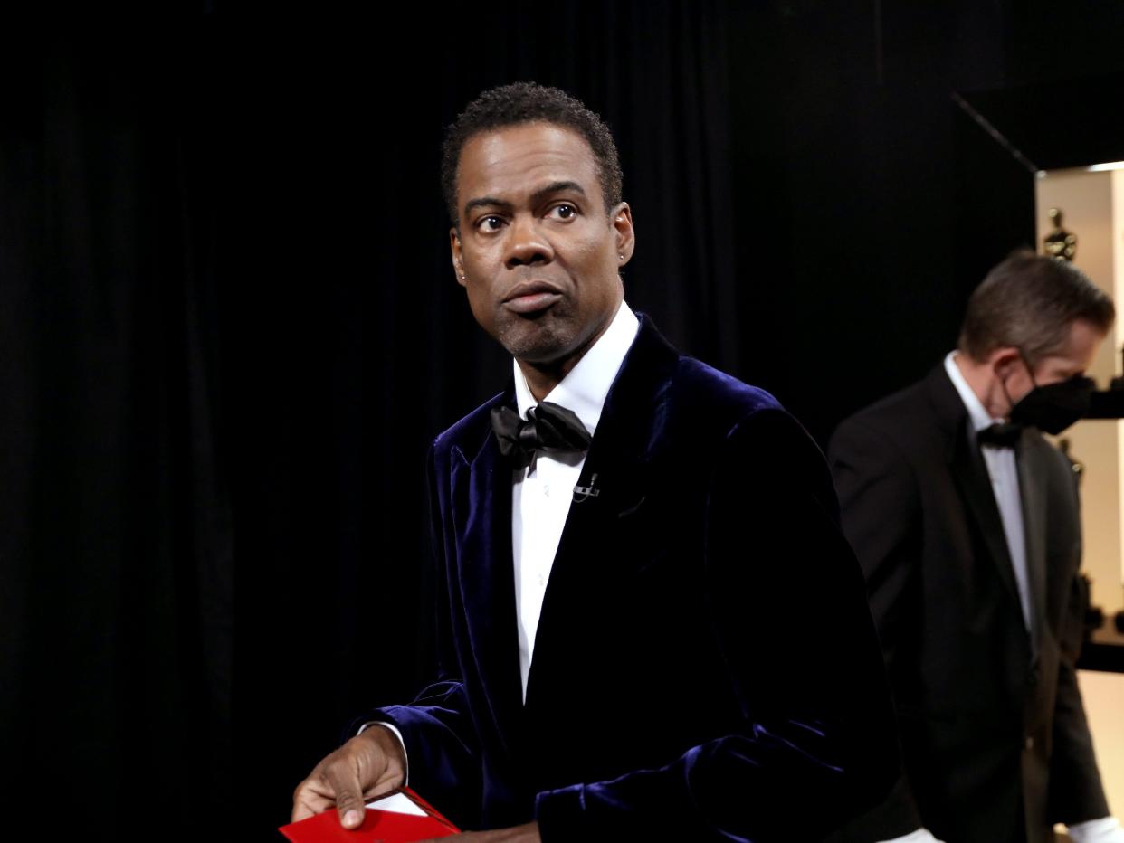 An image of Chris Rock wearing a tuxedo, carrying a red envelope