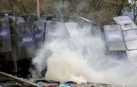 Macedonian police officers try to take cover from tear gas thrown back by a stranded migrant, as minor clashes broke out during a protest against the building of a metal fence at the Greek-Macedonian borders near the village of Idomeni, Greece November 28, 2015. REUTERS/Yannis Behrakis