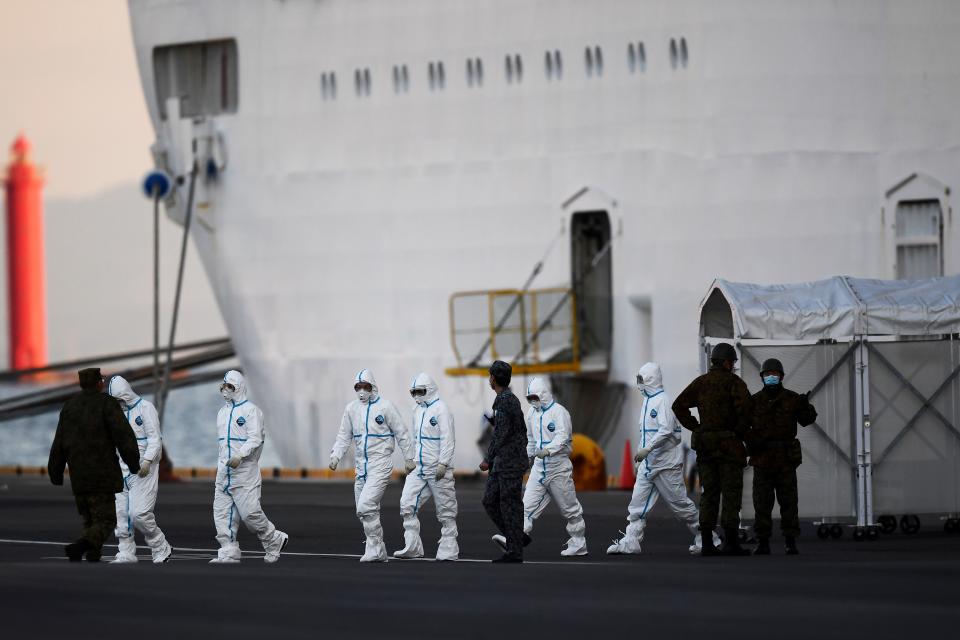 People wearing protective suits walk from the Diamond Princess cruise ship, with around 3,600 people quarantined onboard due to fears of the new coronavirus, at the Daikoku Pier Cruise Terminal in Yokohama port on February 10, 2020. - Around 60 more people on board the quarantined Diamond Princess cruise ship moored off Japan have been diagnosed with novel coronavirus, the country's national broadcaster said on February 10, raising the number of infected passengers and crew to around 130. (Photo by CHARLY TRIBALLEAU / AFP) (Photo by CHARLY TRIBALLEAU/AFP via Getty Images)