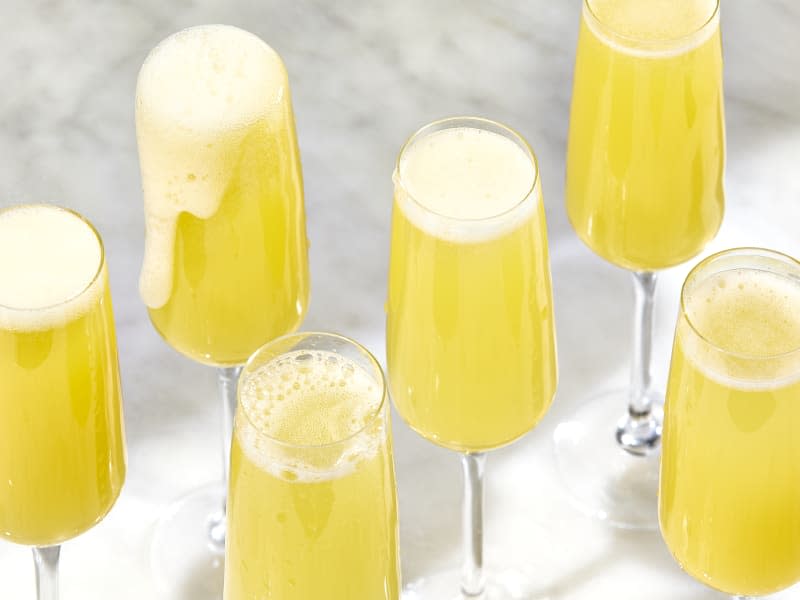 angled shot of five flute glasses with mimosas, on a marble surface.