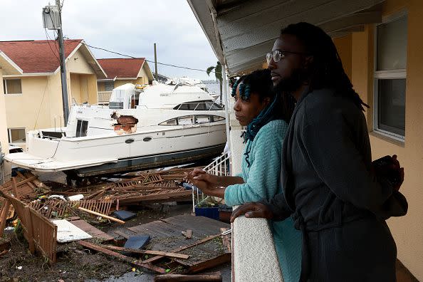 FORT MYERS FLORIDA - SEPTEMBER 29: Frankie Romulus (L) and Kendrick Romulus stand outside of their apartment next to a boat that floated into their apartment complex when Hurricane Ian passed through the area on September 29, 2022 in Fort Myers, Florida. Mrs. Brennan said the boat floated in around 7pm. The hurricane brought high winds, storm surge and rain to the area causing severe damage. (Photo by Joe Raedle/Getty Images)
