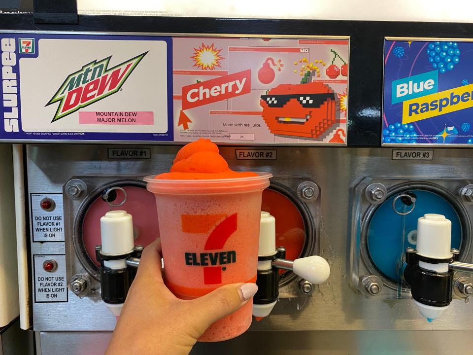 A hand filling up a large 7/11 cup with cherry slurpee