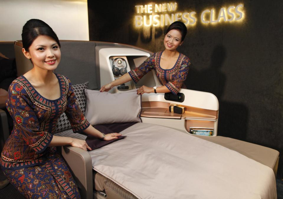 Singapore Airlines Ltd stewardesses pose next to a business class seat during the launch of their new generation of cabin products at Changi Airport in Singapore