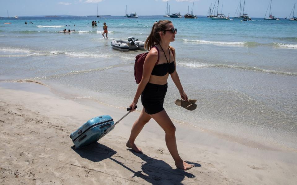 A tourist leaves a beach in Ibiza this month, dragging her suitcase - Zowy Voeten/Getty