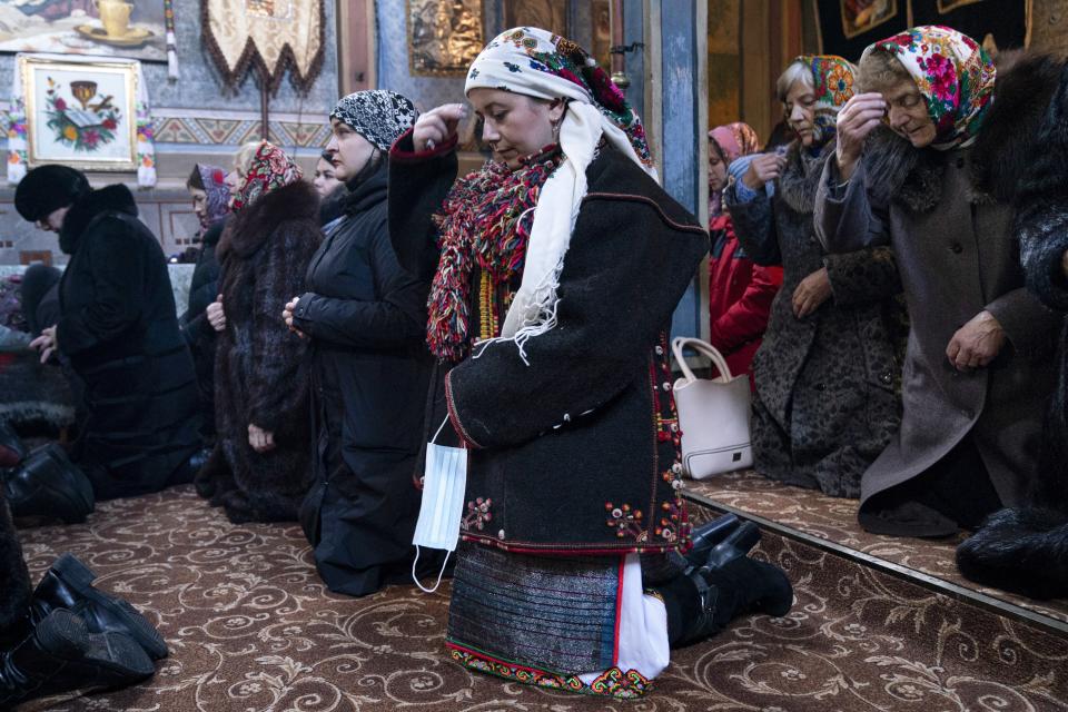 Dr. Viktoria Mahnych, wearing a Hutsul's traditional colorful clothes, crosses herself holding a face mask in her hand because other worshippers forced her to take off her mask " in order not to remind about the contagion" in the Holy Trinity church during the Orthodox Christmas celebration in Iltsi village, Ivano-Frankivsk region of Western Ukraine, Thursday, Jan. 7, 2021. Mahnych fears that a lockdown in Ukraine came too late and the long holidays, during which Ukrainians frequented entertainment venues, attended festive parties and crowded church services, will trigger a surge in new coronavirus infections. (AP Photo/Evgeniy Maloletka)