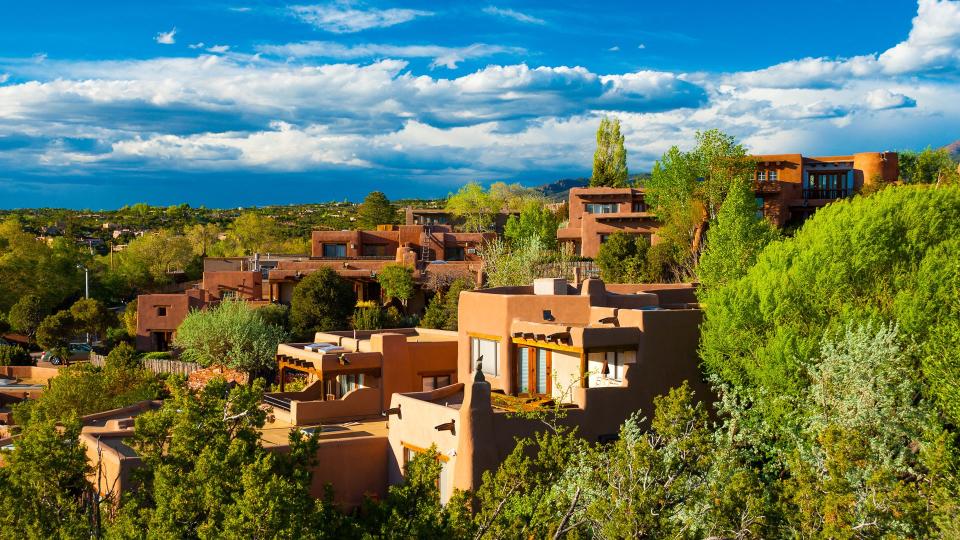 Hillside houses and trees in Santa Fe, New Mexico, with  clouds in the background.