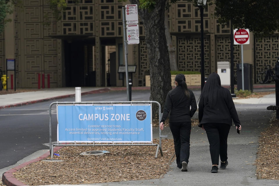 Pedestrian walk past a Campus Zone sign, which advises restricted access to approved students, faculty, staff, essential deliveries, testing and maintenance, on the Stanford University campus in Stanford, Calif., Wednesday, Sept. 2, 2020. With the coronavirus spreading through colleges at alarming rates, universities are scrambling to find quarantine locations in dormitory buildings and off-campus properties to isolate the thousands of students who have caught COVID-19 or been exposed to it. (AP Photo/Jeff Chiu)