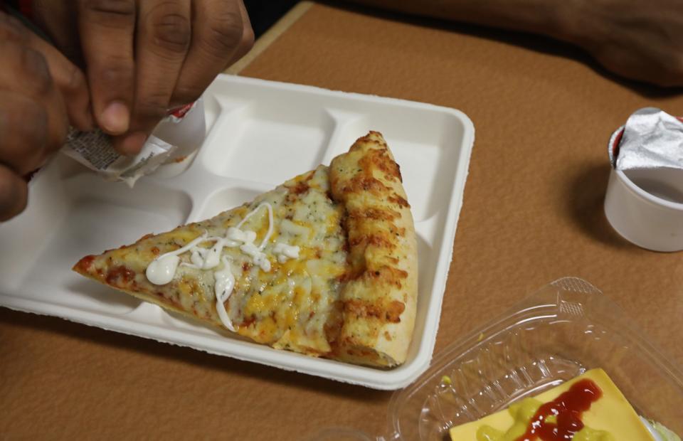 Ke'Sean Chung, a junior at Wilson Magnet High School, covers his slice of pizza with salad dressing during his lunch period in the school cafeteria in Rochester Wednesday, June 8, 2022.