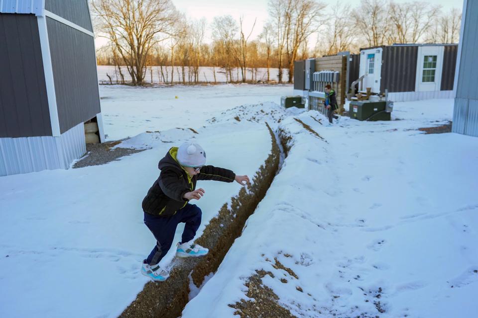 Waylon Prince jumps across a small ditch while playing outside his family's temporary home at Camp Graves, Tuesday, Jan. 16, 2024, in Water Valley, Ky. Two years after the tornado outbreak that killed dozens and leveled much of the real estate in Mayfield, many people, like the Prince family, are still living through another, slower disaster, the search for housing. (AP Photo/Joshua A. Bickel)