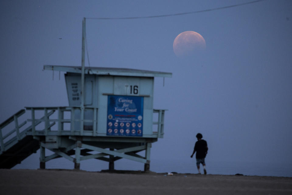 A woman watches as the full-moon sets over Santa Monica Beach in Santa Monica, Calif., Wednesday, May 26, 2021. The first total lunar eclipse in more than two years is coinciding with a supermoon for quite a cosmic show. (AP Photo/Ringo H.W. Chiu)