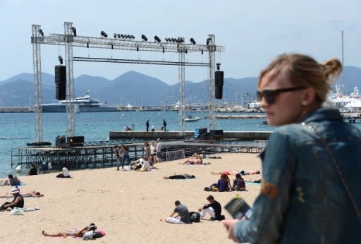People sit on the beach next to a podium where films will be projected on a giant screen on the eve of the 65th Cannes film festival