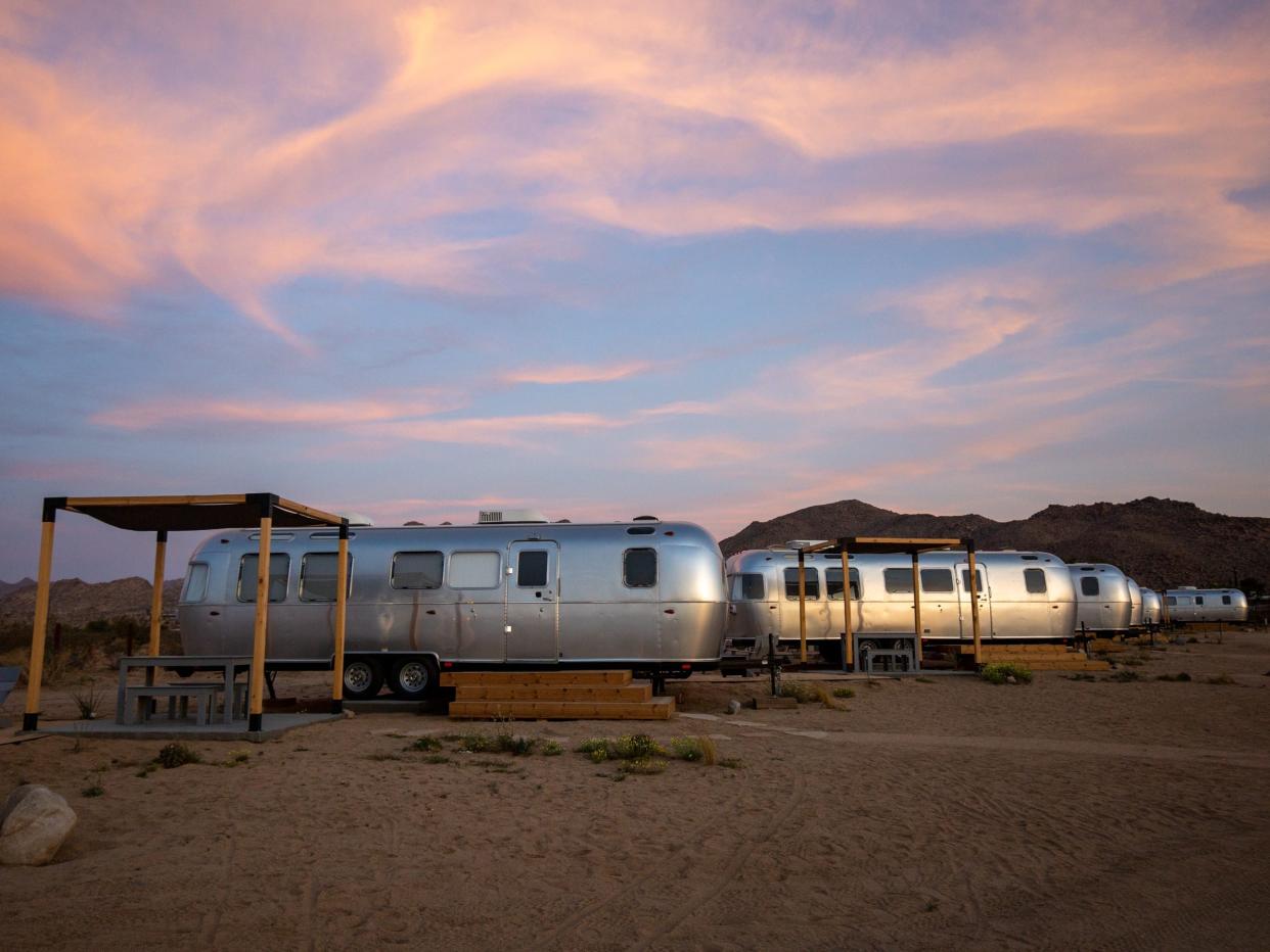 Airstream trailers outside at Autocamp's Joshua Tree location at sunset. There's tables and chairs between each trailer.