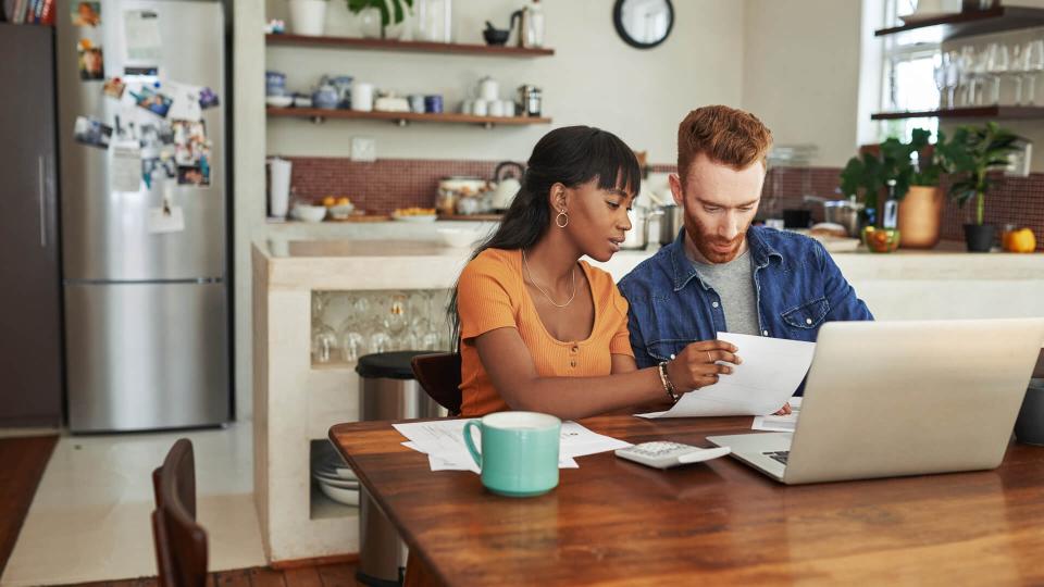 Cropped shot of a couple looking at paperwork while sitting with their laptop.