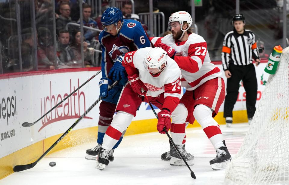 Colorado Avalanche defenseman Erik Johnson, left, fights for control of the puck with Detroit Red Wings left wing Adam Erne (73) and center Michael Rasmussen (27) in the second period at Ball Arena in Denver on Friday, Dec. 10, 2021.