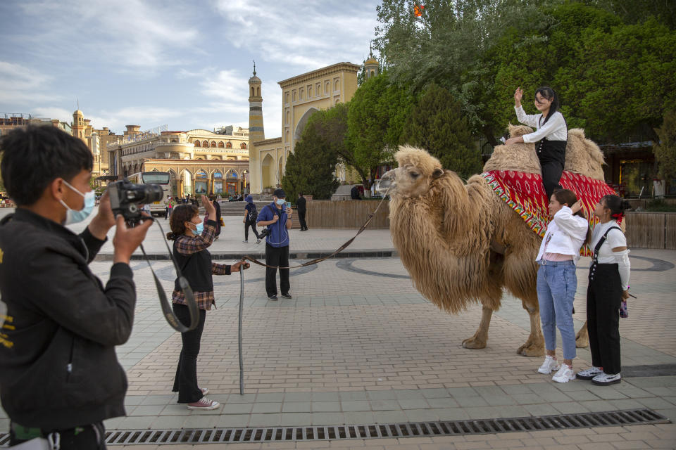 Tourists pose for photos as one of them sits atop a camel outside the Id Kah Mosque in Kashgar northwestern China's Xinjiang Uyghur Autonomous Region, during a government organized visit on April 19, 2021. Four years after Beijing's brutal crackdown on largely Muslim minorities native to Xinjiang, Chinese authorities are dialing back the region's high-tech police state and stepping up tourism. But even as a sense of normality returns, fear remains, hidden but pervasive. (AP Photo/Mark Schiefelbein)