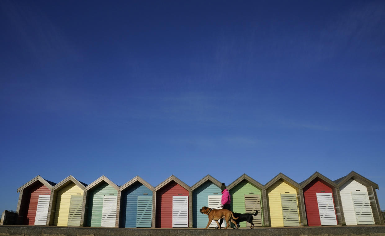 A woman walks her dog past beach huts at Blyth beach in Northumberland 