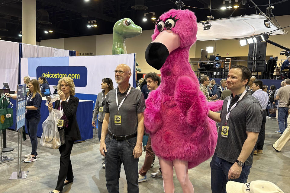 Berkshire Hathaway shareholders pose with the mascot for one of its companies, Oriental Trading, while the more famous spokeslizard for Geico insurance looms over their shoulder, Friday, May 3, 2024, in Omaha, Neb. CEO Warren Buffett will spend hours answering questions at the meeting on Saturday. (AP Photo/Josh Funk)