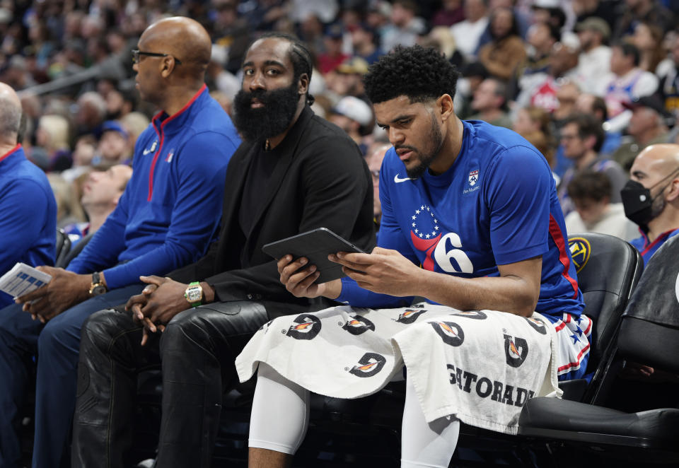 Philadelphia 76ers forward Tobias Harris, front, studies a tablet as injured guard James Harden looks on in the first half of an NBA basketball game against the Denver Nuggets, Monday, March 27, 2023, in Denver. (AP Photo/David Zalubowski)