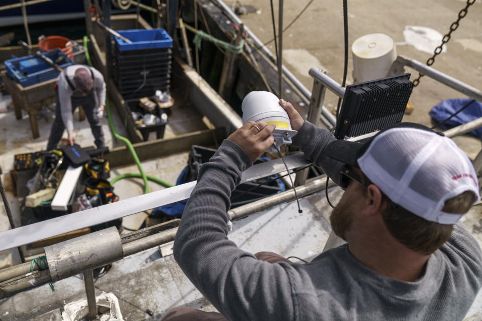 Mark Hager, right, and Anthony Lucia, install a camera aboard the Sabrina Maria fishing vessel in Gloucester, Mass., May 11, 2022. Hager's Maine-based startup, New England Maritime Monitoring, is one of a bevy of companies seeking to help commercial vessels comply with new federal mandates aimed at protecting dwindling fish stocks. But taking the technology overseas, where the vast majority of seafood consumed in the U.S. is caught, is a steep challenge. (AP Photo/David Goldman)