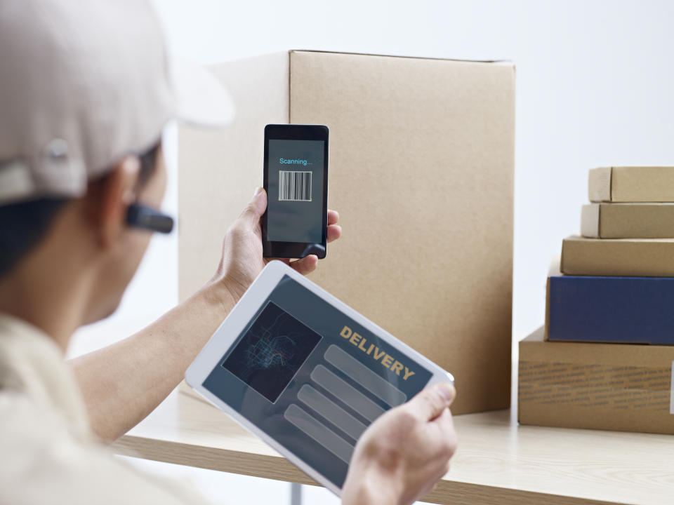 male asian courier company worker using cellphone and tablet computer to scan information on packages.