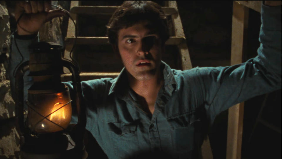 Bruce Campbell holding a lantern while walking down the stairs in The Evil Dead.