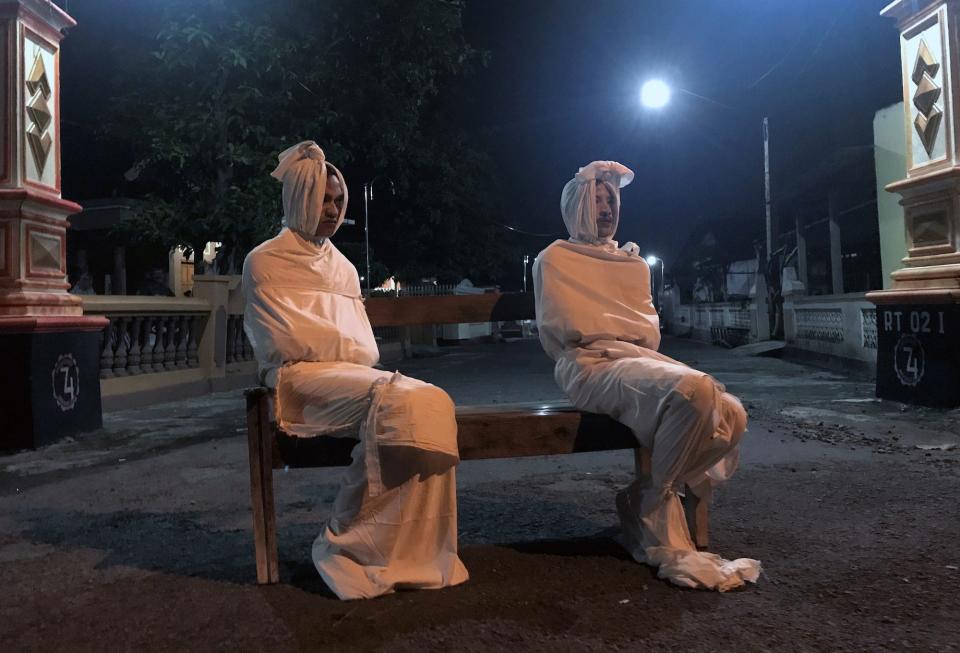 Two volunteers sit on a bench as they play the role of 'pocong', or known as 'shroud ghost', to make people stay at home amid the spread of coronavirus in Indonesia on April 1.