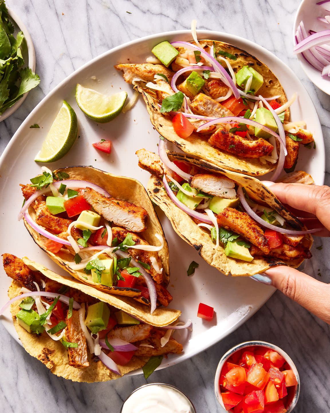 flour tortillas on a plate filled with chicken, tomatoes, avocado and red onion