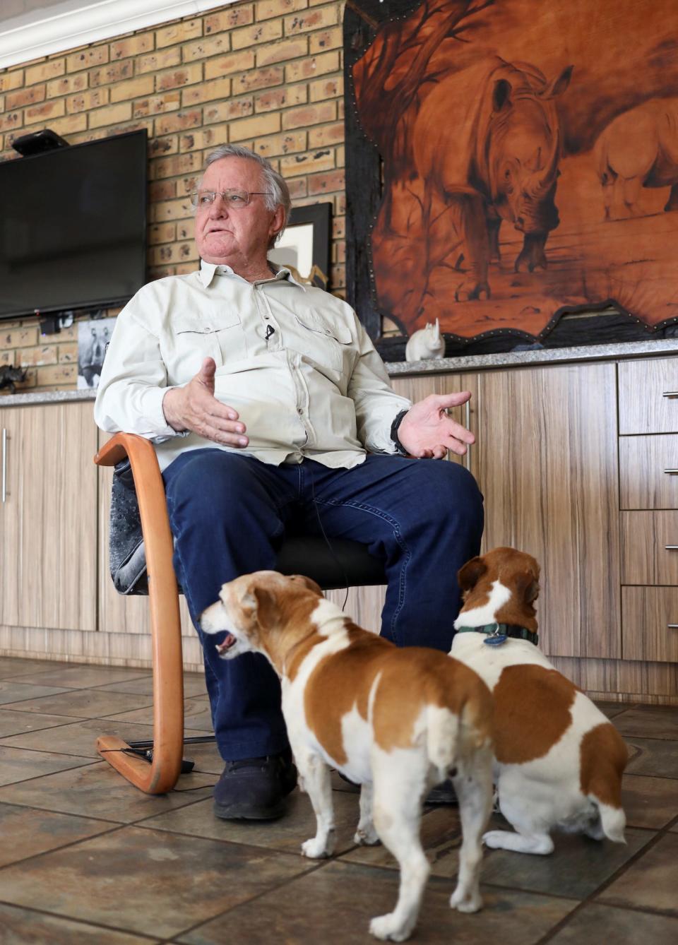 John Hume, private rhino breeder, looks on while sitting in a chair with two dogs at his feet.