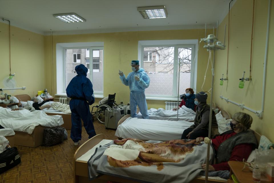 A medical worker talks with coronavirus patients in a hospital organized in the medical college in Lviv, Western Ukraine, on Monday, Jan. 4, 2021. A medical college in western Ukraine has been transformed into a temporary hospital as the coronavirus inundates the Eastern European country. The foyer of the college in the city of Lviv holds 50 beds for COVID-19 patients, and 300 more were placed in lecture halls and auditoriums to accommodate the overflow of people seeking care at a packed emergency hospital nearby. . (AP Photo/Evgeniy Maloletka)