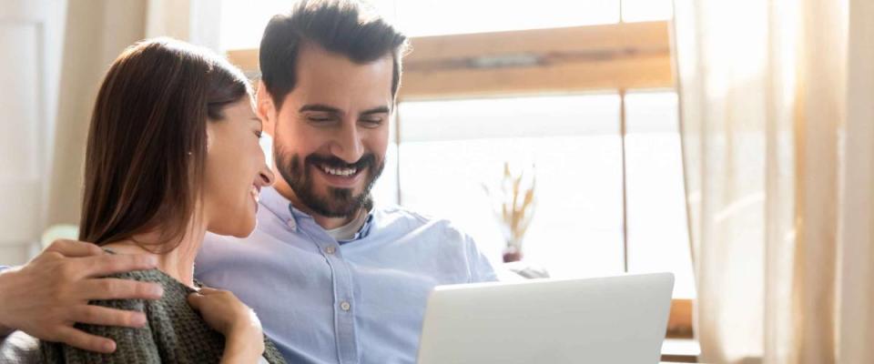 Man and woman smiling while using laptop on the couch