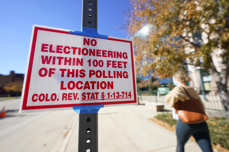 FILE - In this Oct. 30, 2020, file photo, a sign warns against electioneering as a voter walks by to cast her ballot in the atrium of Ball Arena, the home of the NBA's Denver Nuggets and the NHL's Colorado Avalanche in Denver. Voters in Colorado, Florida and Alabama passed ballot measures Tuesday, Nov. 3, that codify what is already law: That only U.S. citizens 18 and older can vote. The passage of the largely-symbolic measures has triggered questions about why the pro-Trump group behind them spent time and money on the effort. (AP Photo/David Zalubowski, File)