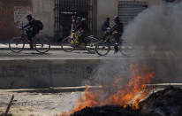 Commuters on bicycles ride past a barricade set up by protesters against the postponement of the presidential election in El Alto, Bolivia, Monday, Aug. 10, 2020. Citing the ongoing new coronavirus pandemic, the nation's highest electoral authority delayed presidential elections from Sept. 6 to Oct. 18, the third time the vote has been delayed. (AP Photo/Juan Karita)