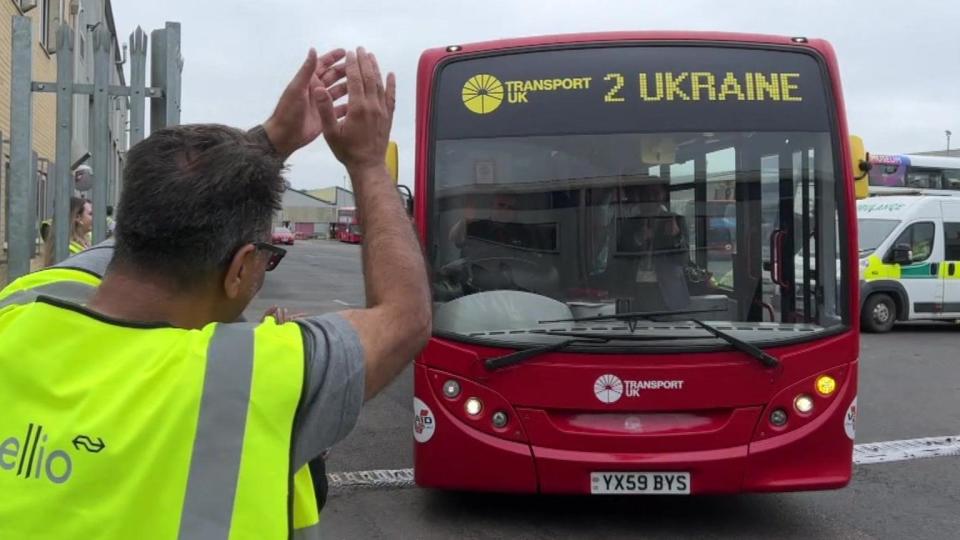 A red bus with 'Ukraine' on the windscreen being cheered by a man in a hi-vis vest