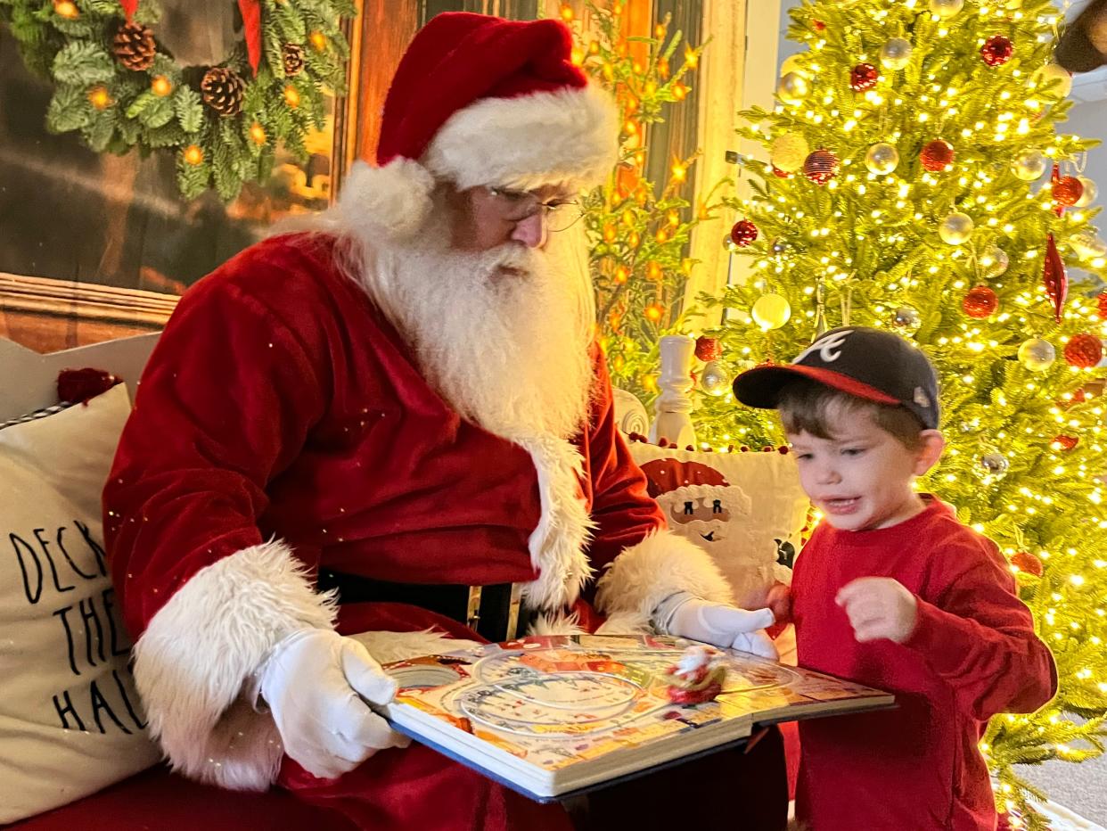 FILE - Two-year-old James Prescott and Santa Claus, portrayed by Burt Rayburn, play with the "Busy Santa" book featuring a toy Santa in a sleigh zooming across the pages during a "Sensory Santa" event at Flack Family Chiropractic in Evans. The event will be brought back on Dec. 2.